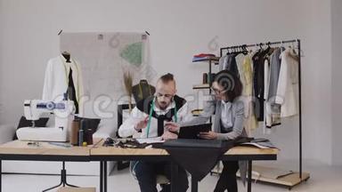 时装设计师在办公室工作，使用不同的裁剪工具和衣服。 两位时装设计师男女